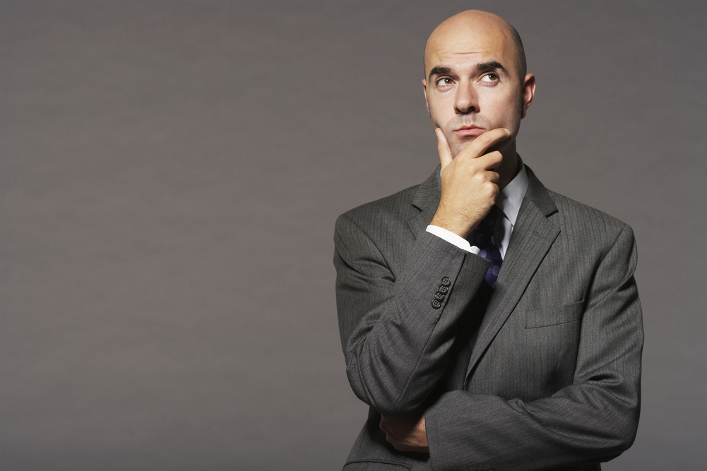 bald-businessman-with-hand-on-chin-thinking-against-gray-background